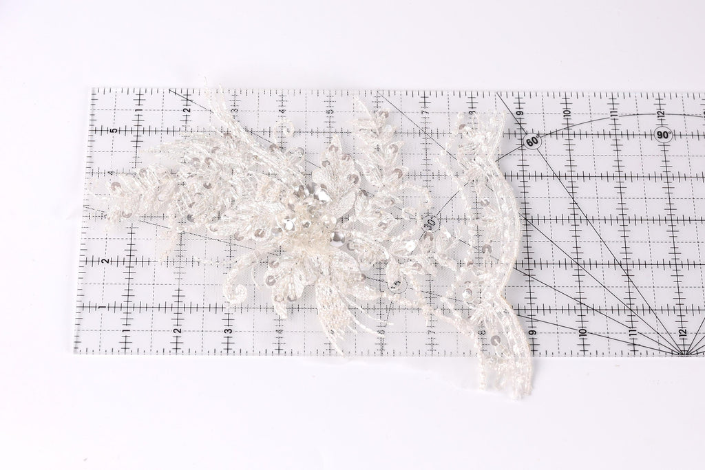 a piece of white lace with intricate patterns, placed on a transparent ruler.