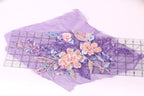 a close-up view of a purple fabric with a floral design, including pink and blue flowers and leaves. The fabric is spread out on a ruler, which is placed on a white surface.