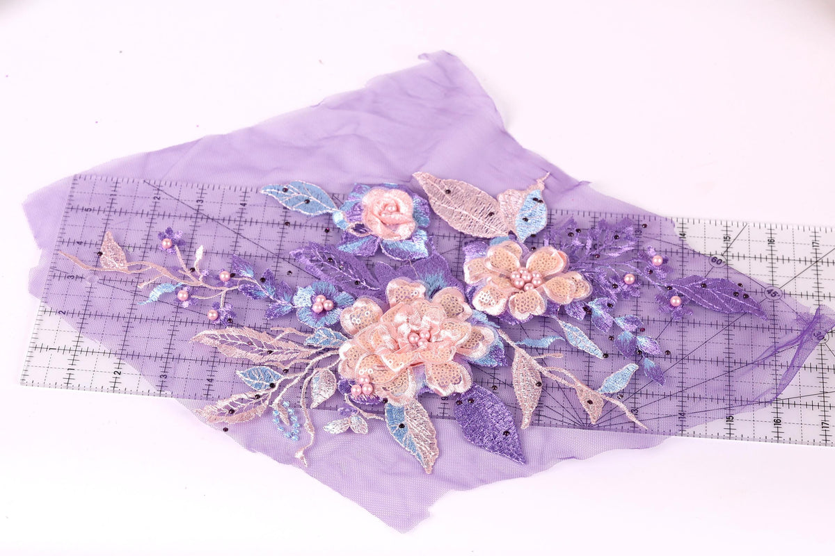 a close-up view of a purple fabric with a floral design, including pink and blue flowers and leaves. The fabric is spread out on a ruler, which is placed on a white surface.