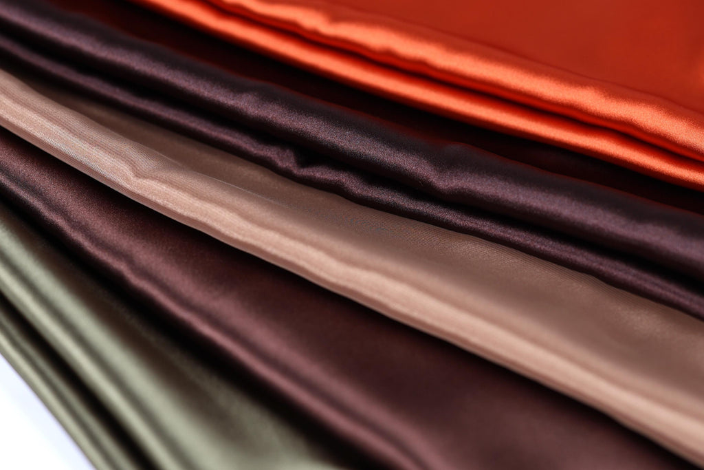 A close-up image of various colored satin fabrics, including red, brown, and green, arranged in a visually appealing manner.