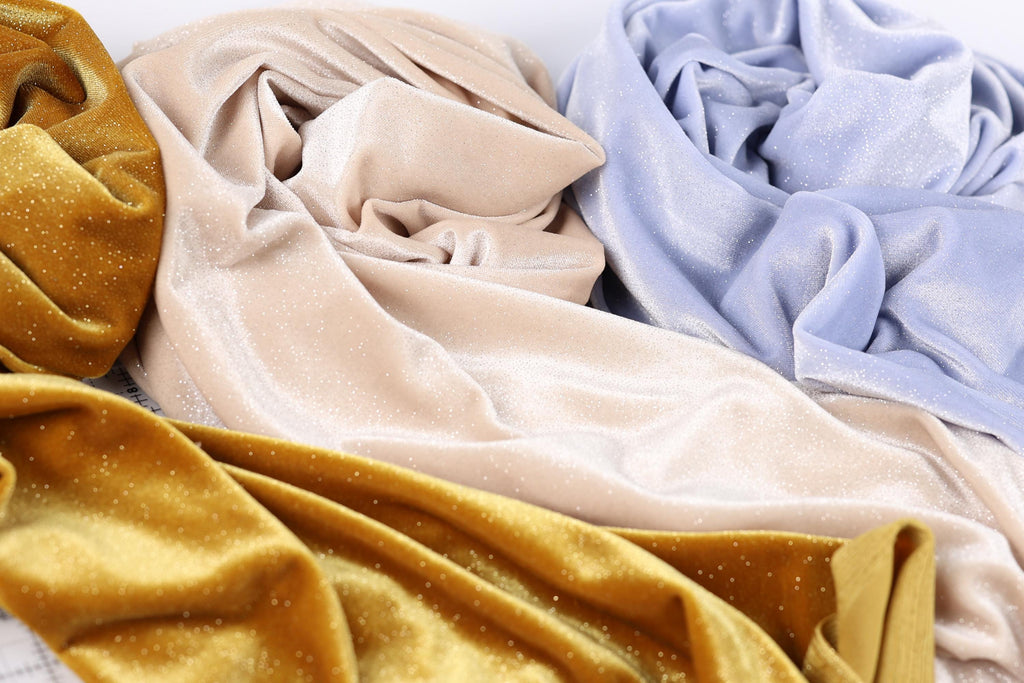 a close-up view of three different fabric swatches, each with a unique color and texture. The fabric appears to be made of velvet, with a shiny, glittery appearance. The swatches are arranged in a way that allows for a clear comparison of their colors and textures.