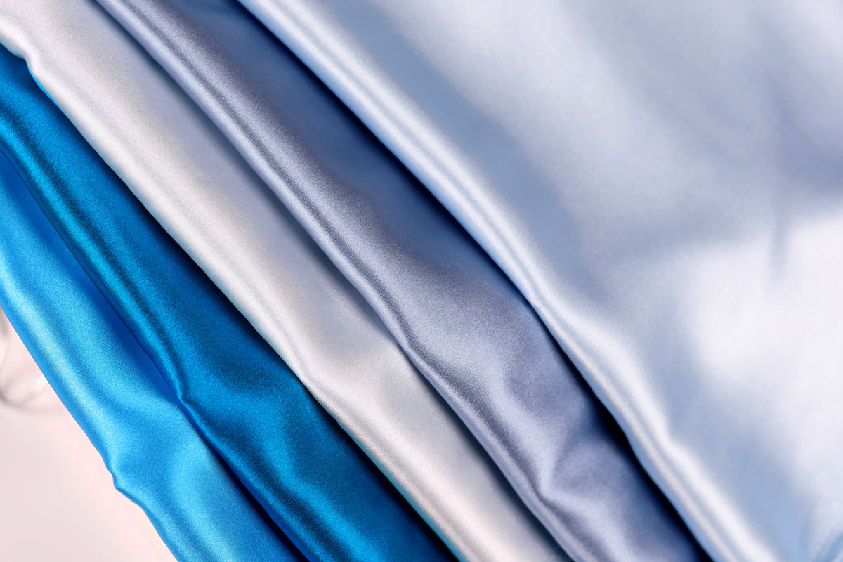 A close-up image of four different colored satin fabrics, with the colors being blue, gray, and white.