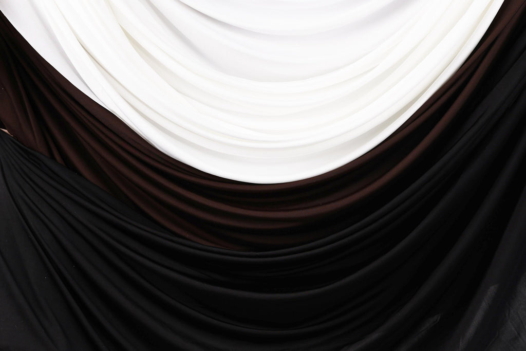 a close-up view of a fabric with three distinct colors: white, brown, and black. The fabric appears to be made of a soft, flowing material, possibly silk or chiffon, and is draped or folded in a way that creates a visually appealing pattern.