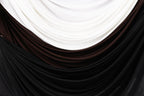 a close-up view of a fabric with three distinct colors: white, brown, and black. The fabric appears to be made of a soft, flowing material, possibly silk or chiffon, and is draped or folded in a way that creates a visually appealing pattern.