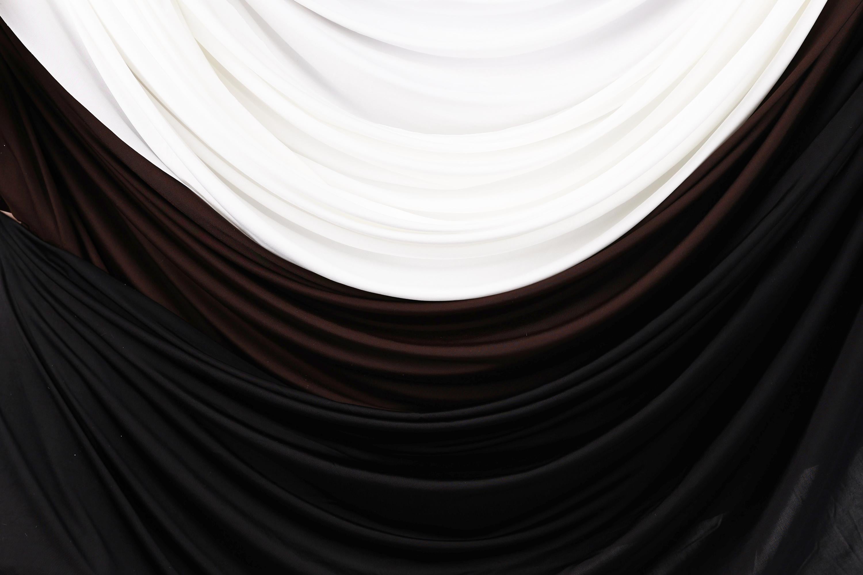 a close-up view of a fabric with three distinct colors: white, brown, and black. The fabric appears to be made of a soft, flowing material, possibly silk or chiffon, and is draped or folded in a way that creates a visually appealing pattern.