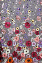 a close-up view of a fabric with a vibrant floral pattern. The fabric is adorned with a variety of colorful flowers, including red, pink, white, and yellow flowers, as well as purple and orange flowers. The flowers are intricately embroidered or sewn onto the fabric, creating a visually striking and detailed design. The image does not contain any text or other discernible objects, and the focus is solely on the floral pattern on the fabric.
