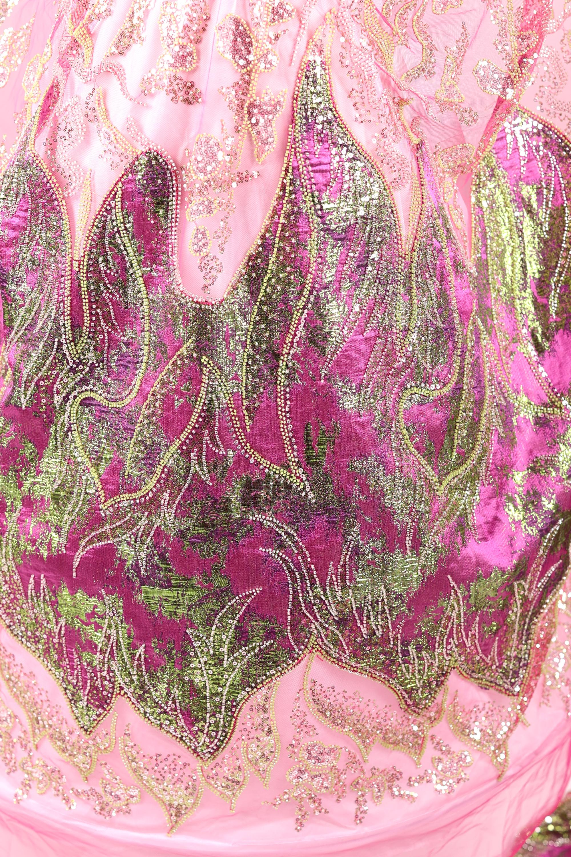 The image is a close-up of a pink and green sequined dress, showcasing intricate patterns and designs.
