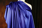 A close-up view of a blue satin fabric draped over a mannequin, with a dark background.