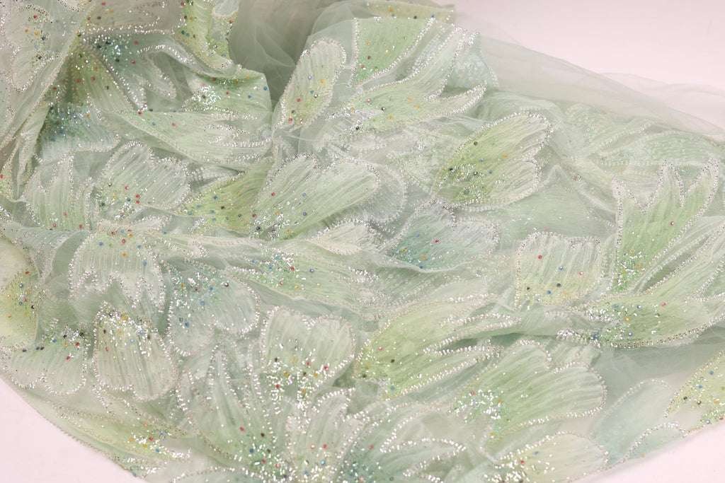 a close-up view of a fabric with a floral pattern, featuring green and white colors and small, colorful beads or sequins on the surface.
