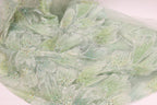 a close-up view of a fabric with a floral pattern, featuring green and white colors and small, colorful beads or sequins on the surface.
