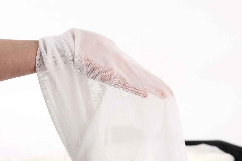 A hand is holding a white fabric, possibly a sheer or sheer-like material, against a plain white background.