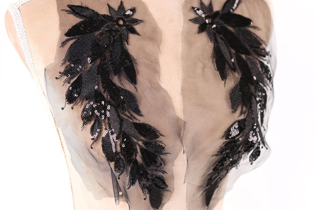 a close-up view of a mannequin torso with intricate black and beige embroidered details, including feathers and sequins, adorning the clothing.