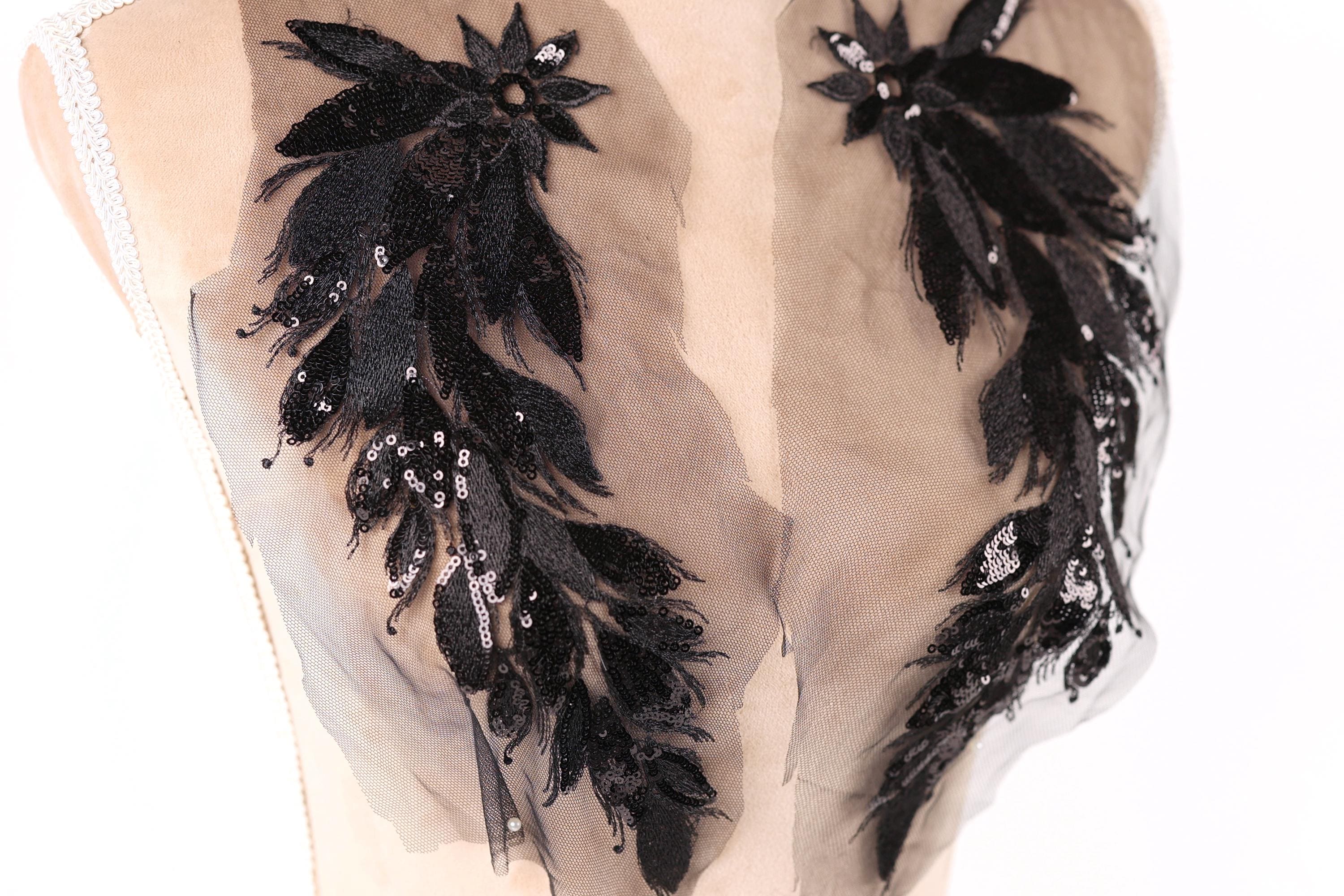 a close-up view of a mannequin torso with intricate black and beige embroidered details, including feathers and sequins, adorning the clothing.