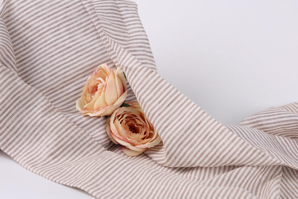 Two delicate pink roses resting on a striped fabric.