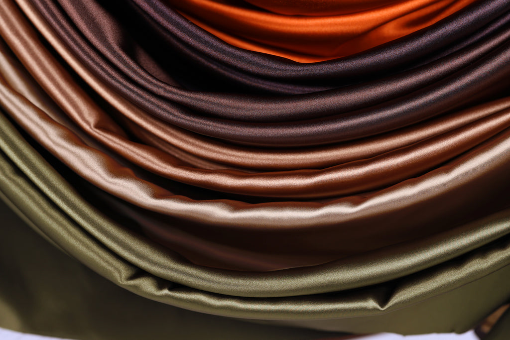 The image is a close-up of a pile of colorful satin fabric, with various shades of brown, orange, and green.