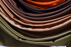 The image is a close-up of a pile of colorful satin fabric, with various shades of brown, orange, and green.