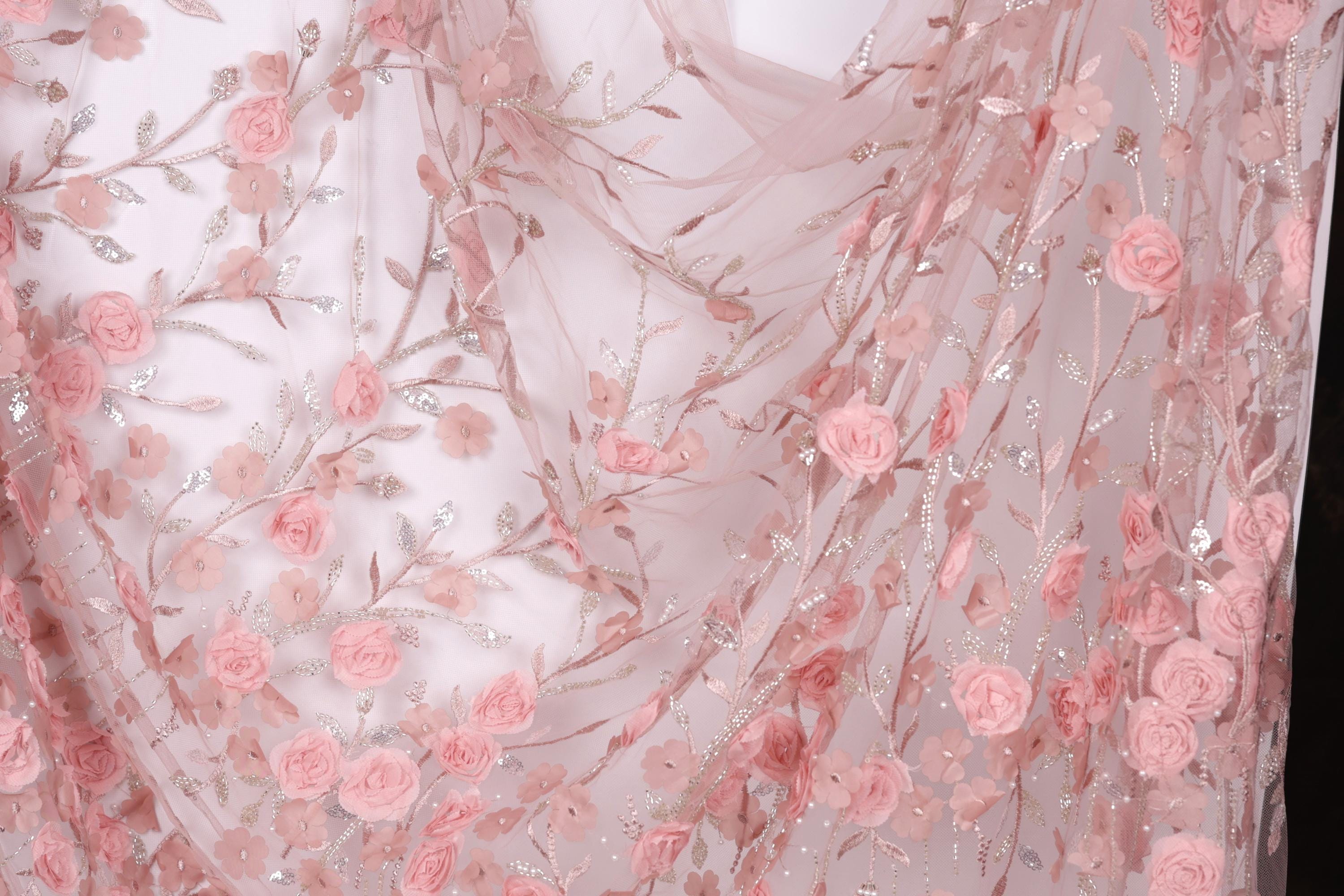 a close-up view of a delicate, pink floral fabric with numerous small pink roses and leaves. The fabric appears to be made of sheer material, giving it a delicate and airy appearance. The roses and leaves are intricately embroidered, adding a touch of elegance and detail to the fabric.
