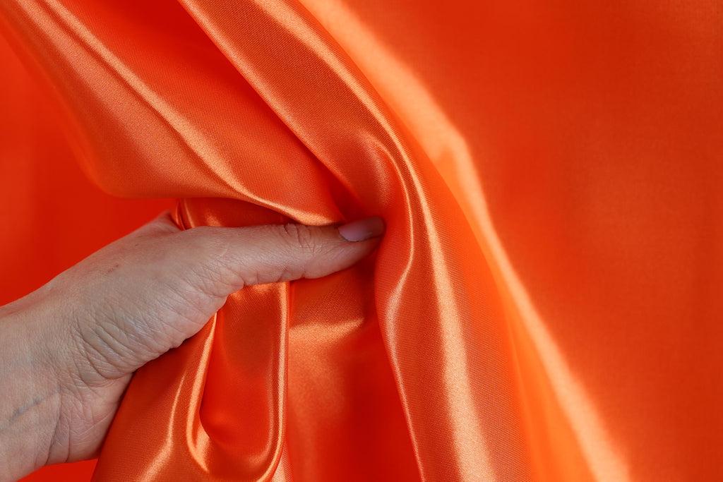 A hand is holding a piece of orange satin fabric, with the fabric partially draped over the hand.