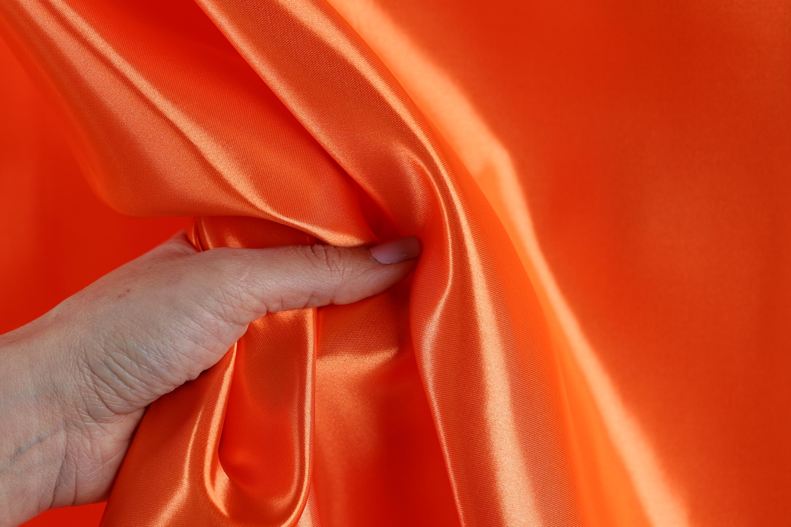 A hand is holding a piece of orange satin fabric, with the fabric partially draped over the hand.