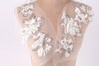 A mannequin wearing a dress with delicate white and silver floral embroidery on the shoulders and neck.