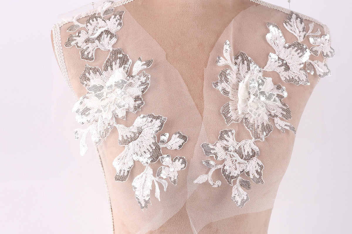 A mannequin wearing a dress with delicate white and silver floral embroidery on the shoulders and neck.