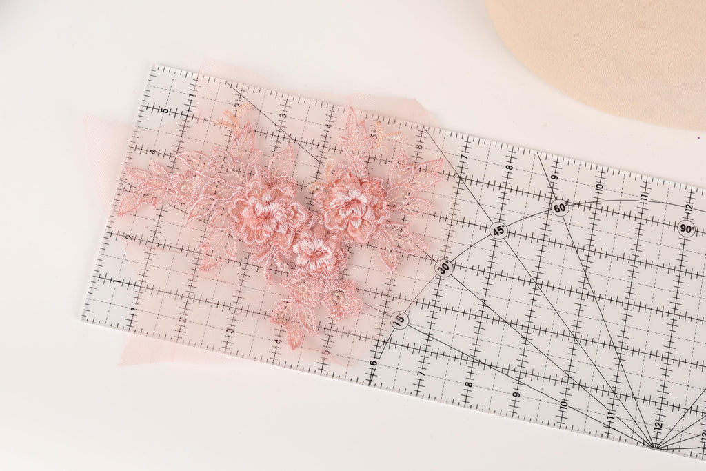a clear ruler with a pink floral design placed on it, indicating that the ruler is being used for measuring or cutting fabric.