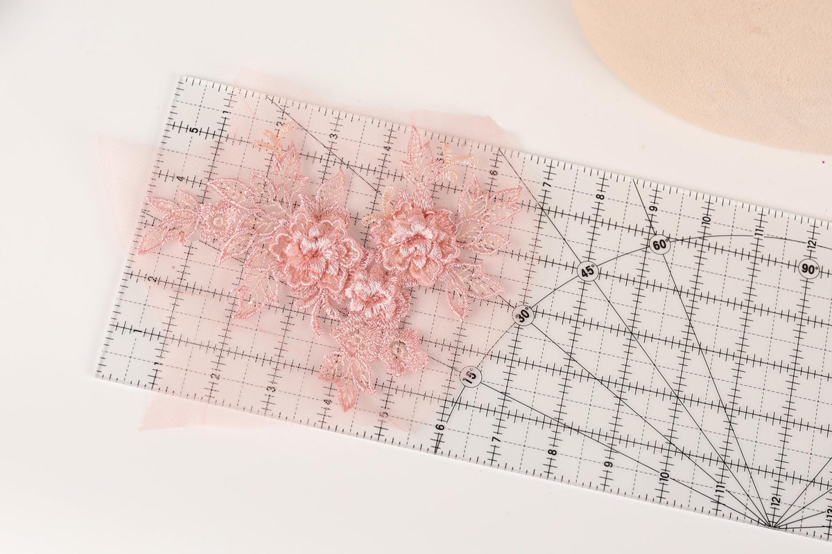 a clear ruler with a pink floral design placed on it, indicating that the ruler is being used for measuring or cutting fabric.