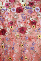 The image is a close-up of a fabric with a vibrant floral pattern, featuring a variety of colorful flowers such as red, pink, yellow, purple, and white. The flowers are intricately embroidered or sewn onto the fabric, creating a visually striking and detailed design.