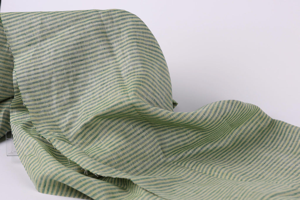 A close-up view of a fabric with green and white striped patterns, appearing crumpled and folded.