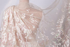 a close-up view of a delicate, sheer fabric with a floral pattern. The fabric appears to be made of lace or a similar delicate material, and it is draped over a mannequin or a model's shoulder. The fabric is flowing and billowing, creating a sense of movement and elegance.