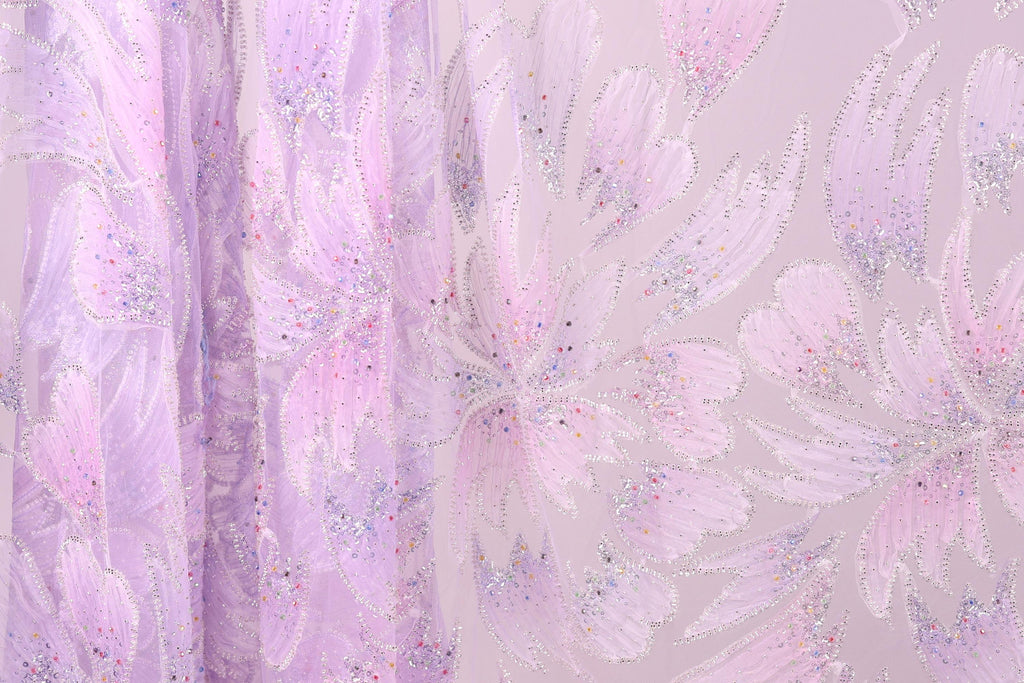 a close-up view of a fabric with a floral pattern in shades of pink and purple. The fabric appears to be made of a sheer material, with a delicate and intricate design. The pattern consists of multiple flowers and leaves, creating a visually appealing and textured appearance.