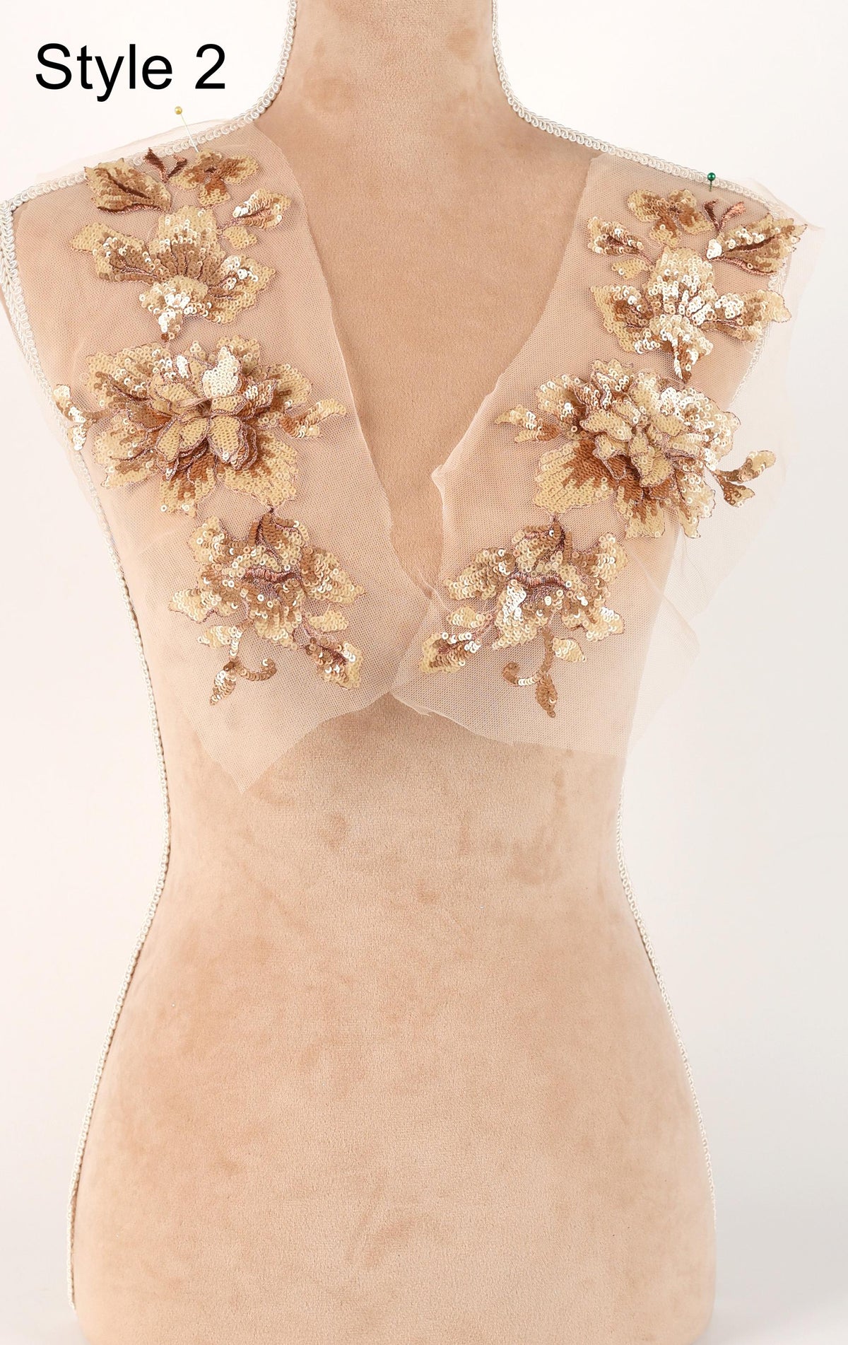 A mannequin with a beige dress featuring intricate gold and white floral embroidery on the shoulders and neckline.