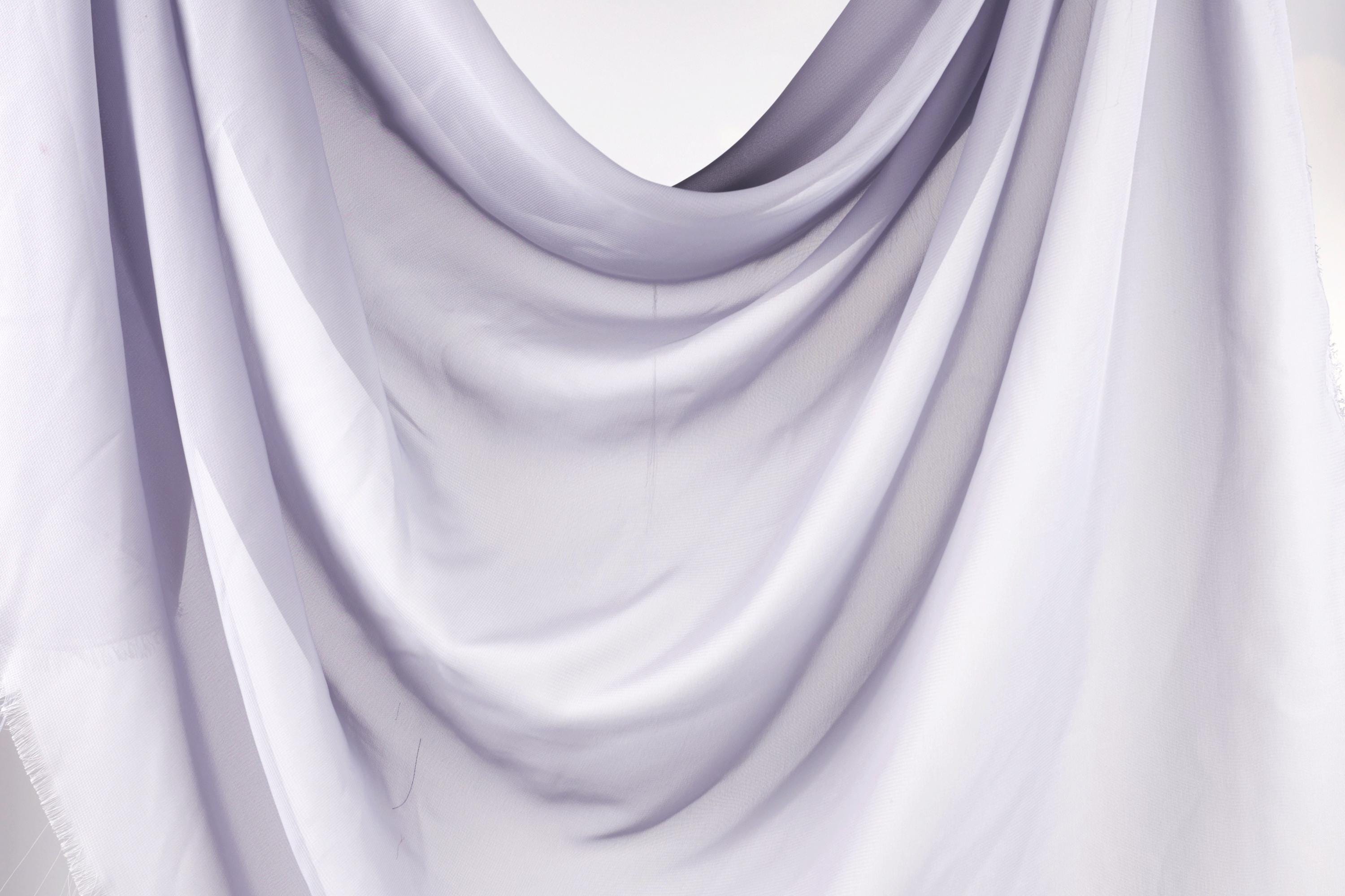 The image is a close-up of a white fabric, possibly a sheer or sheer-like material, with a soft, flowing texture.