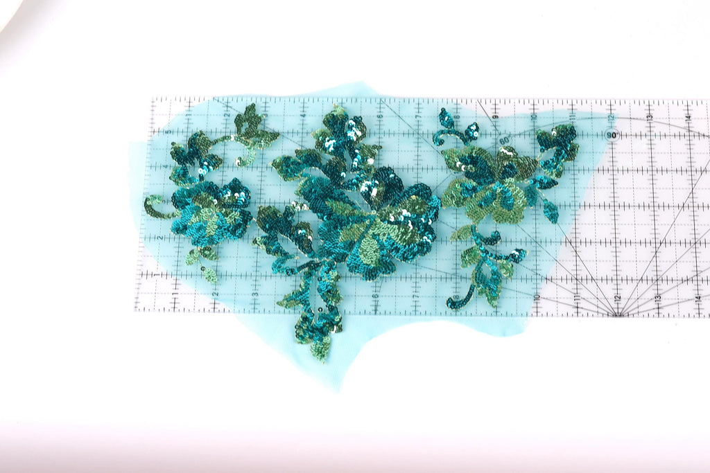 a collection of green and blue sequin designs, including flowers and leaves, arranged on a transparent surface.
