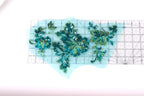 a collection of green and blue sequin designs, including flowers and leaves, arranged on a transparent surface.