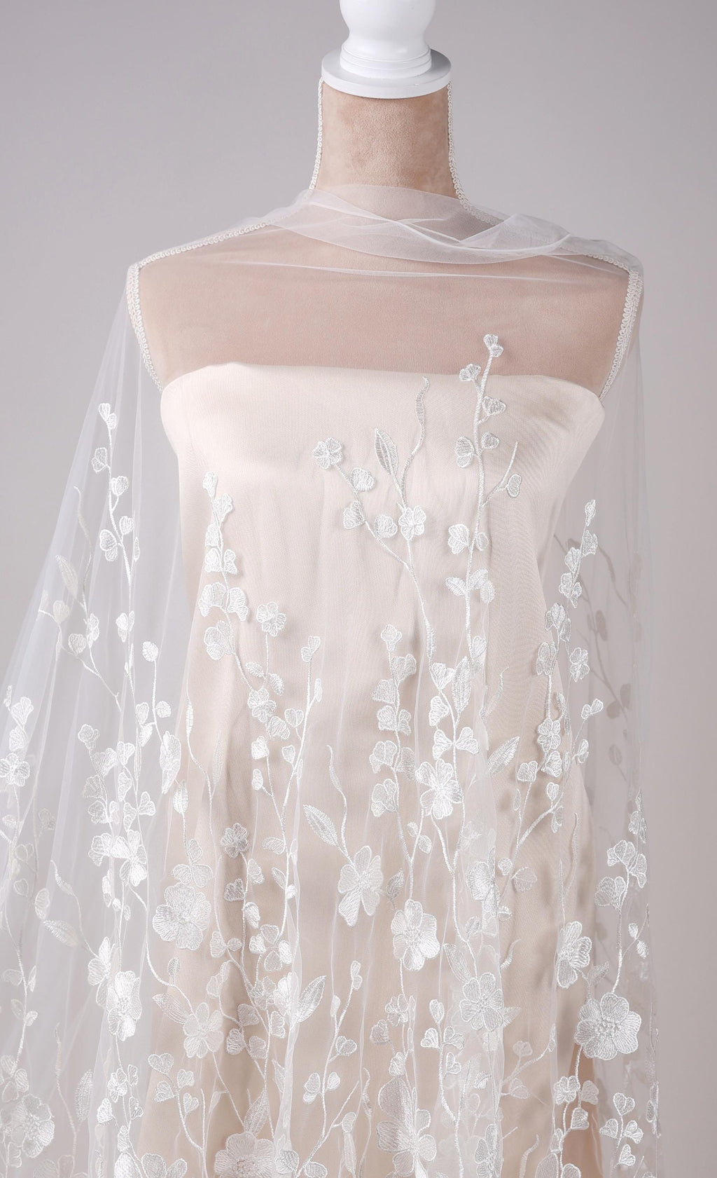 A mannequin wearing a white dress with a sheer, floral-patterned fabric draped over it.