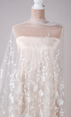A mannequin wearing a white dress with a sheer, floral-patterned fabric draped over it.