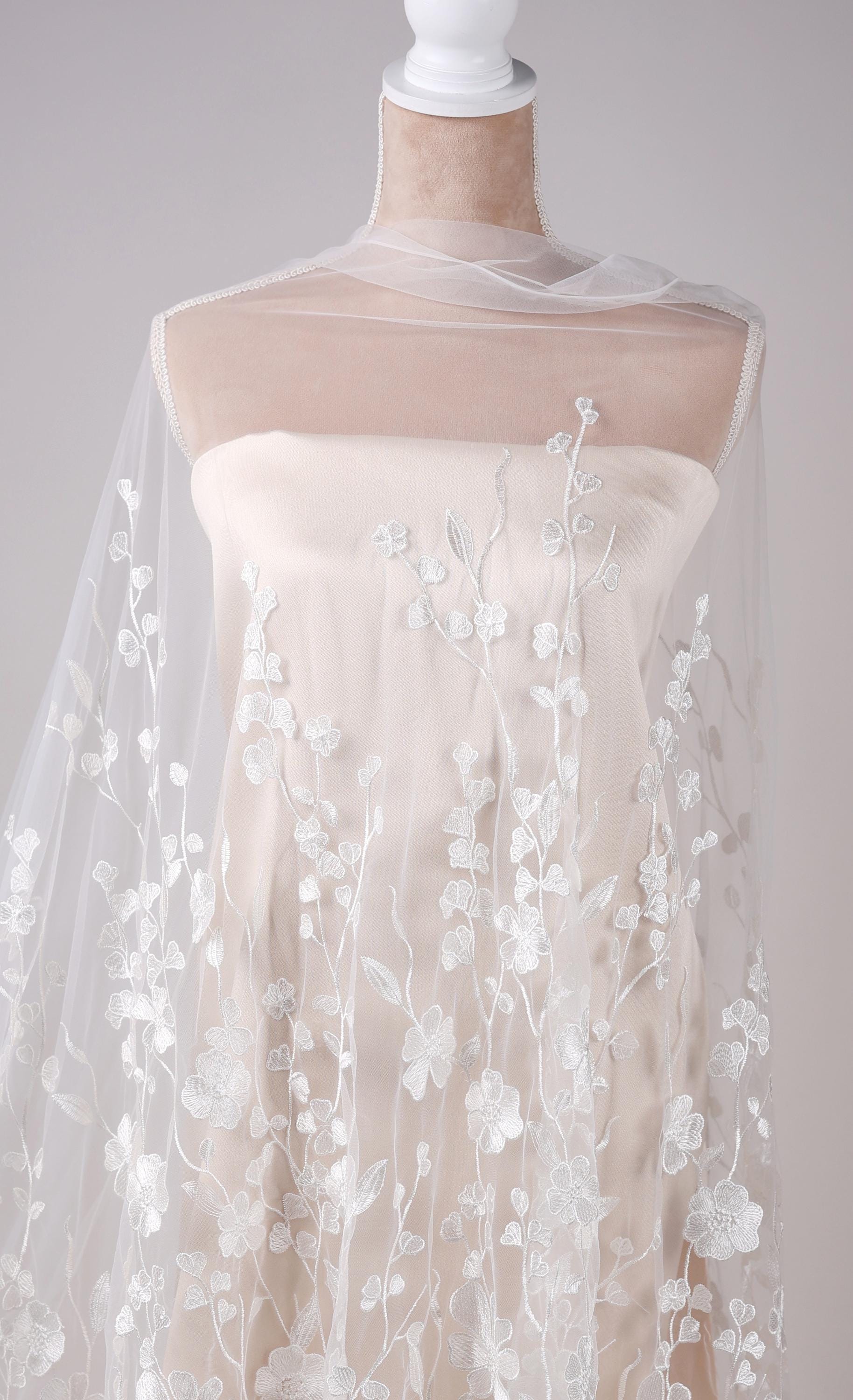A mannequin wearing a white dress with a sheer, floral-patterned fabric draped over it.