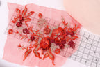a close-up view of a pink fabric adorned with red and gold embroidered flowers and leaves. The fabric is spread out on a pink background, and a ruler is placed next to it, likely for measuring or cutting purposes.
