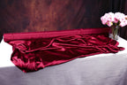 a red satin fabric draped over a white tablecloth, with a vase of pink flowers placed next to it.