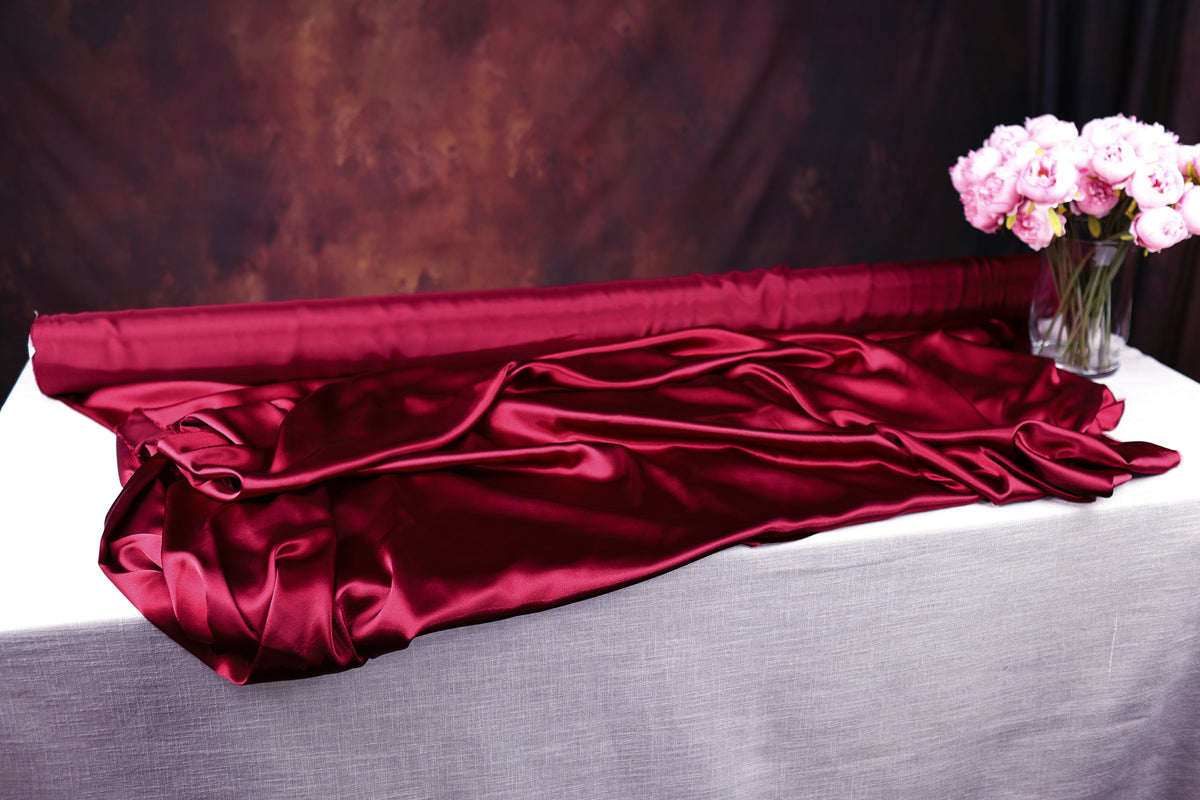 a red satin fabric draped over a white tablecloth, with a vase of pink flowers placed next to it.