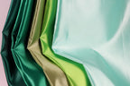 A close-up view of a collection of colorful satin fabric, with a variety of vibrant colors including green, gold, and turquoise.