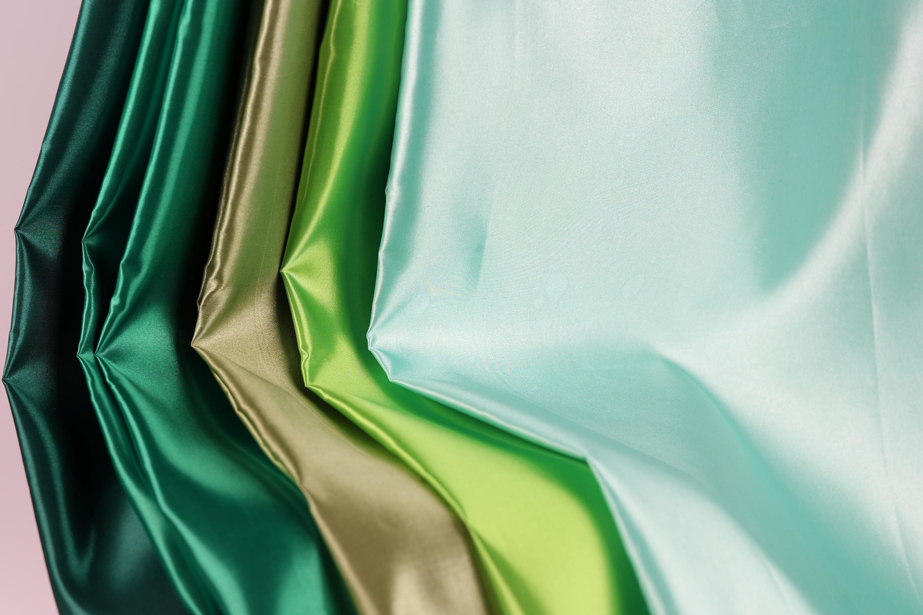 A close-up view of a collection of colorful satin fabric, with a variety of vibrant colors including green, gold, and turquoise.