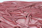 A close-up view of a crumpled, pink velvet fabric, with its folds and creases visible.