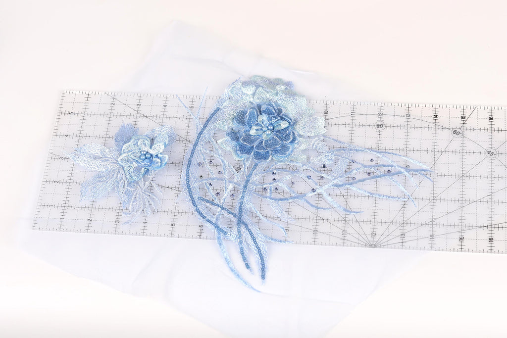 a close-up view of a blue flower-like object with long, thin petals, placed on a transparent ruler.
