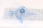 a close-up view of a blue flower-like object with long, thin petals, placed on a transparent ruler.