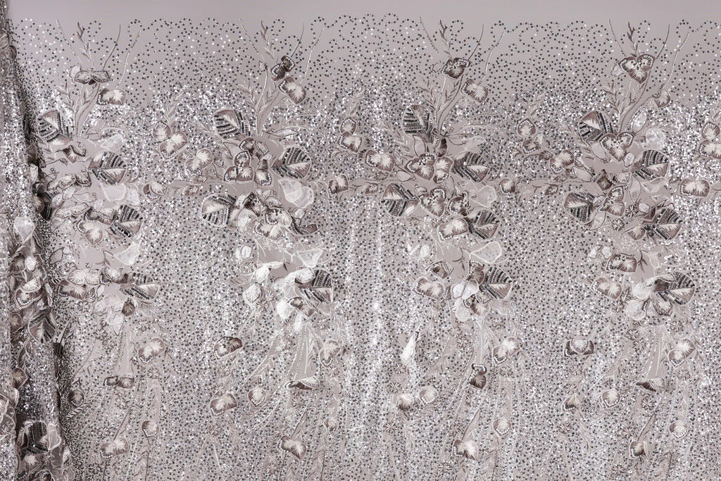 The image is a close-up of a fabric with a repeating pattern of silver and white flowers or leaves, creating a visually striking and intricate design.