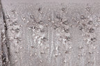 The image is a close-up of a fabric with a repeating pattern of silver and white flowers or leaves, creating a visually striking and intricate design.