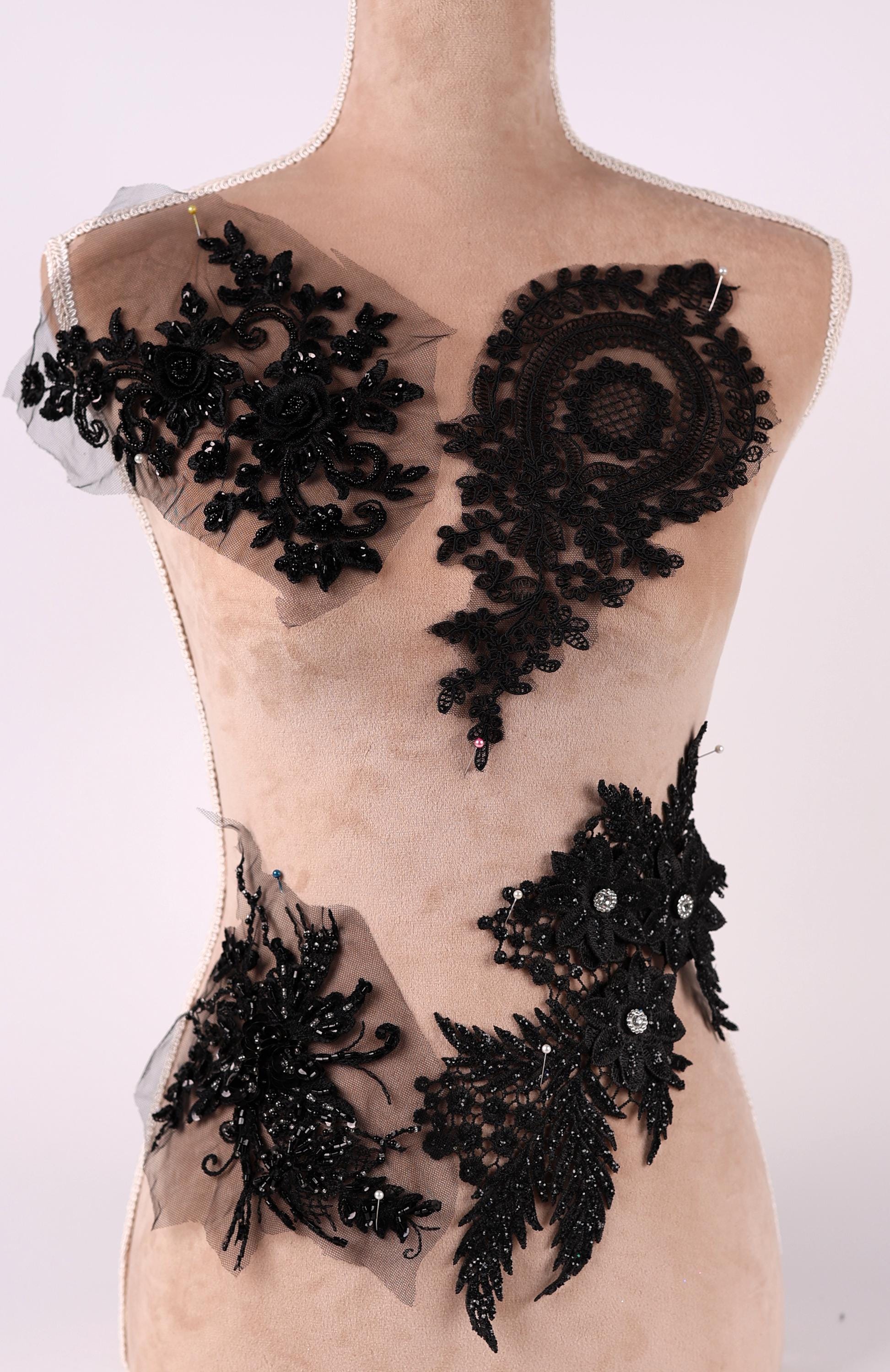 A mannequin wearing a beige dress with various black lace and floral embellishments attached to it.