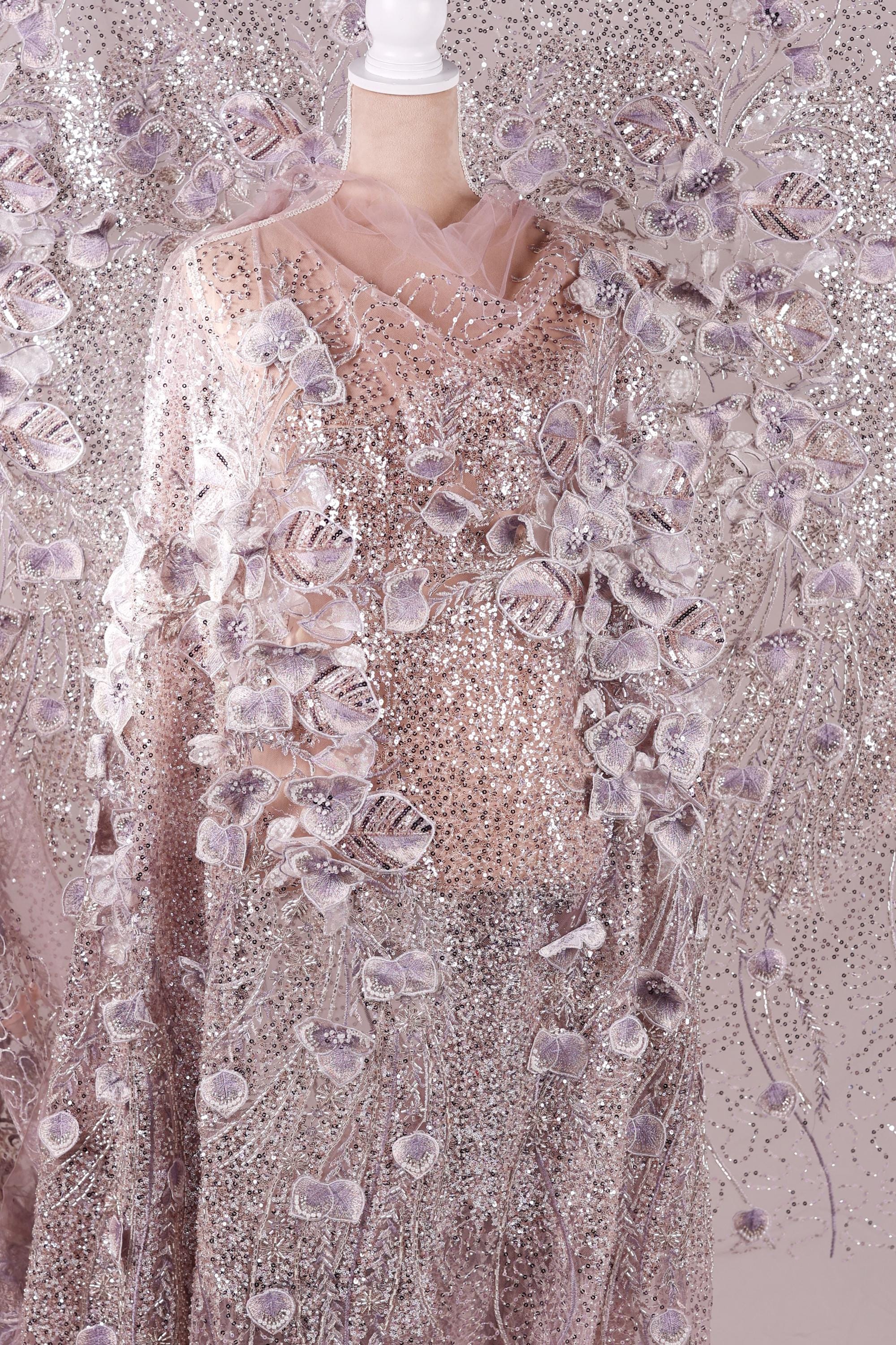 a mannequin wearing a long, flowing dress with a shimmering, sequined bodice and a sheer, floral-patterned skirt. The dress appears to be made of a sheer fabric, giving it a delicate and elegant appearance.